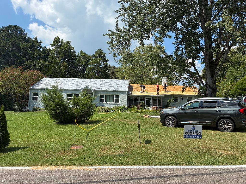Iron Bull Roofing crew installing a new roof with our yard sign in the front lawn