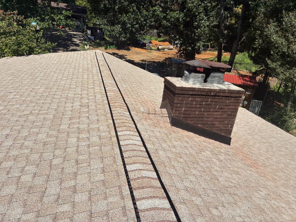 Close-up of a finished roof with tan architectural shingles around a brick chimney