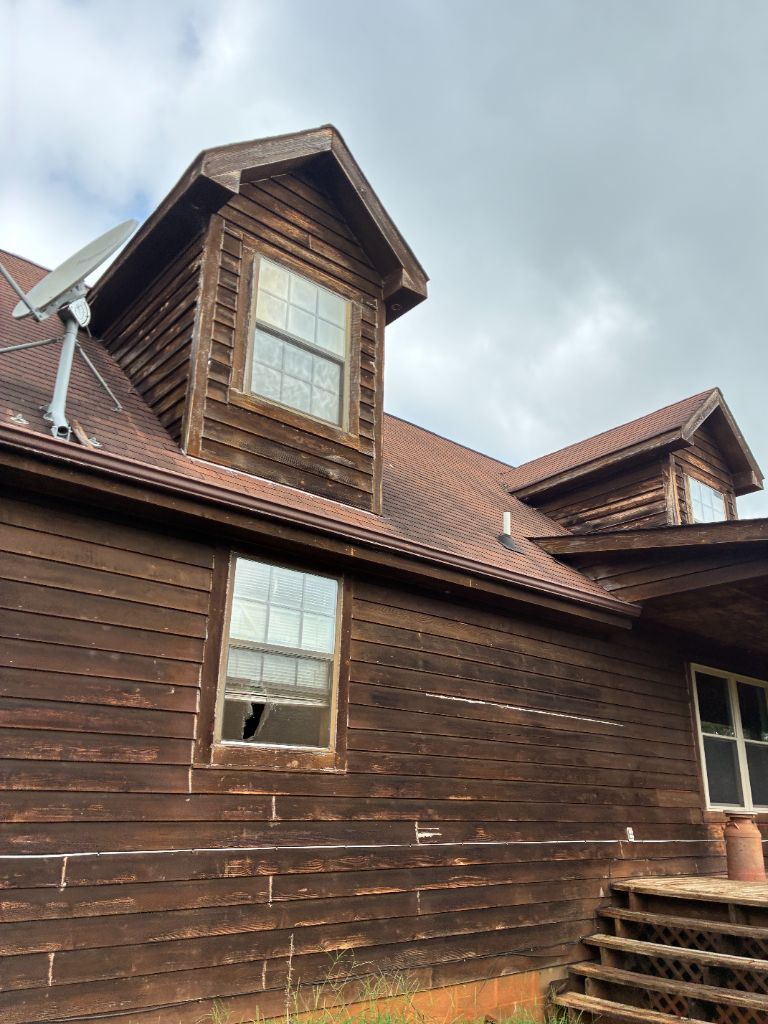 Close-up storm damage inspection on the log home roof, including a broken window pane, ahead of a full re-roof