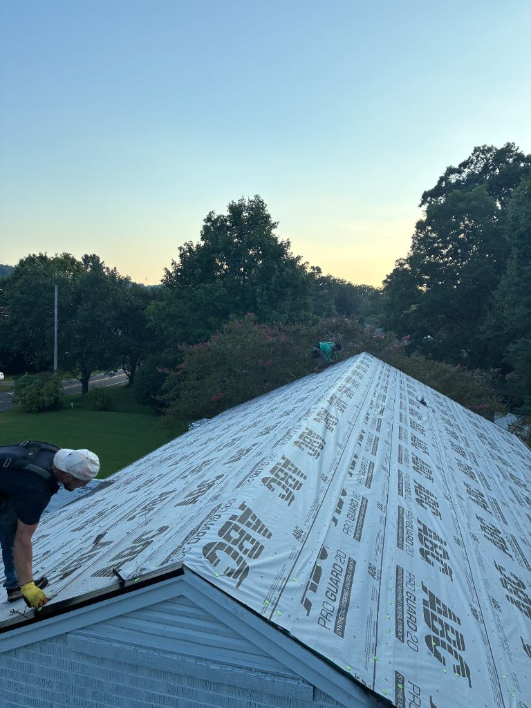 Crew installing white synthetic underlayment on a roof at dusk